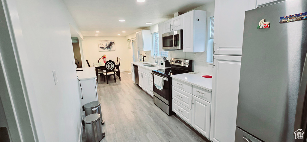 Kitchen with sink, appliances with stainless steel finishes, white cabinetry, tasteful backsplash, and light hardwood / wood-style floors