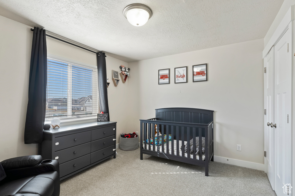Bedroom featuring a textured ceiling, a crib, carpet, and baseboards