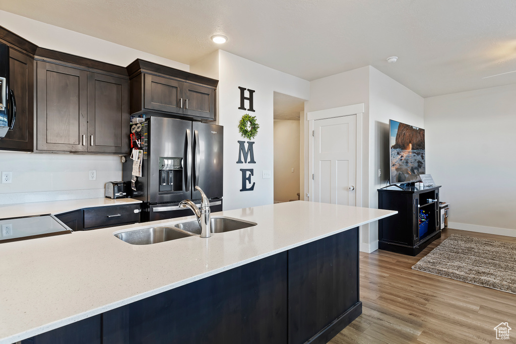 Kitchen featuring dark brown cabinetry, a sink, baseboards, stainless steel refrigerator with ice dispenser, and light wood finished floors