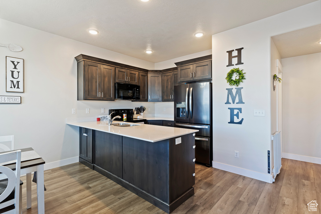 Kitchen with a peninsula, a sink, dark brown cabinets, light countertops, and black appliances