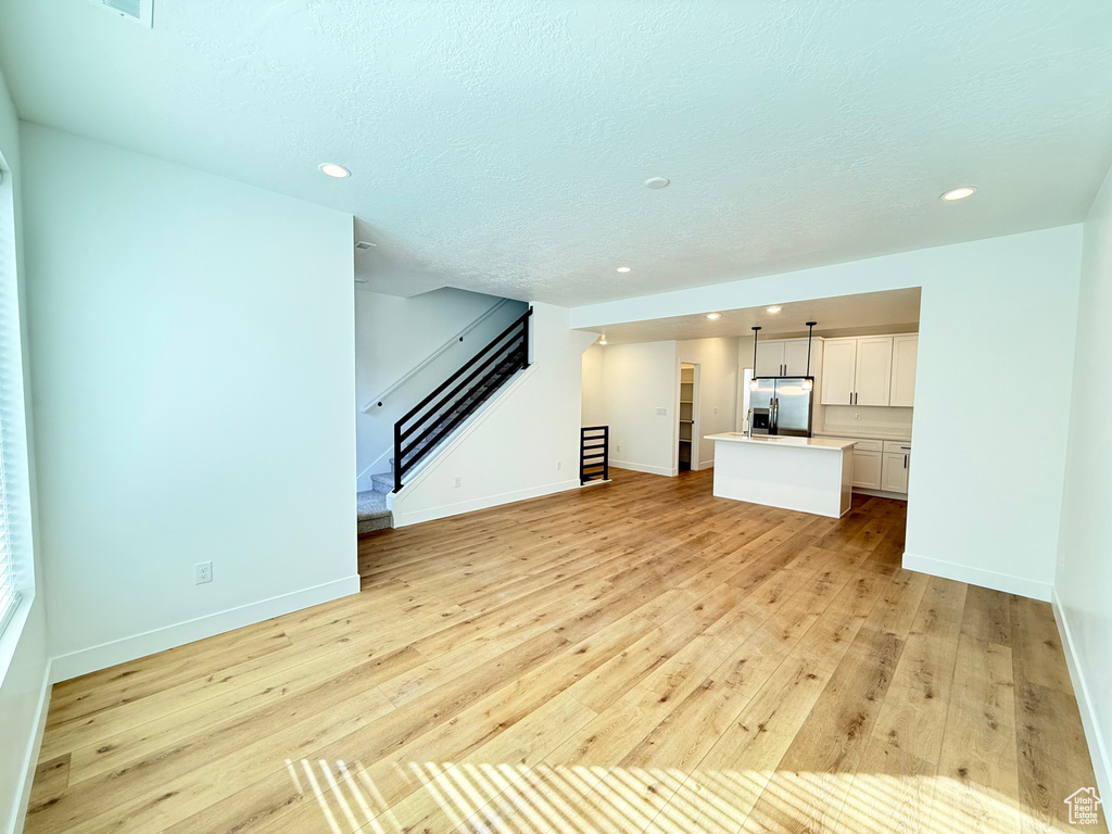 Unfurnished living room with a textured ceiling, light wood-style flooring, recessed lighting, baseboards, and stairway