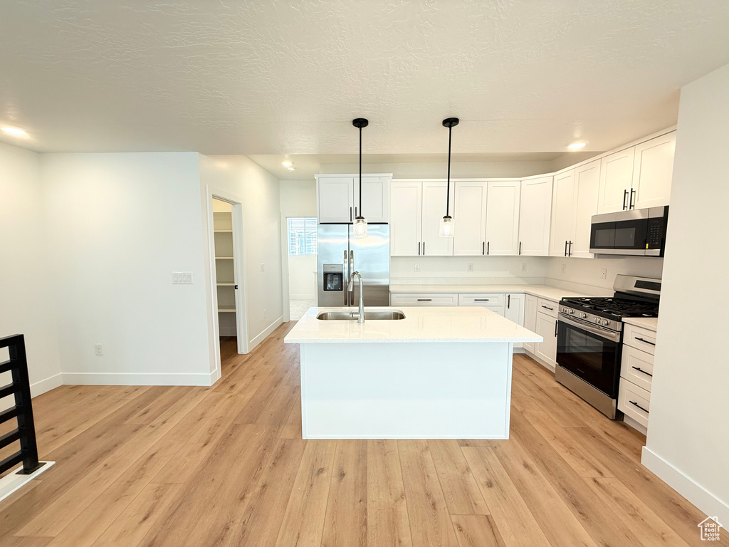 Kitchen with stainless steel appliances, a sink, white cabinets, light countertops, and light wood-type flooring