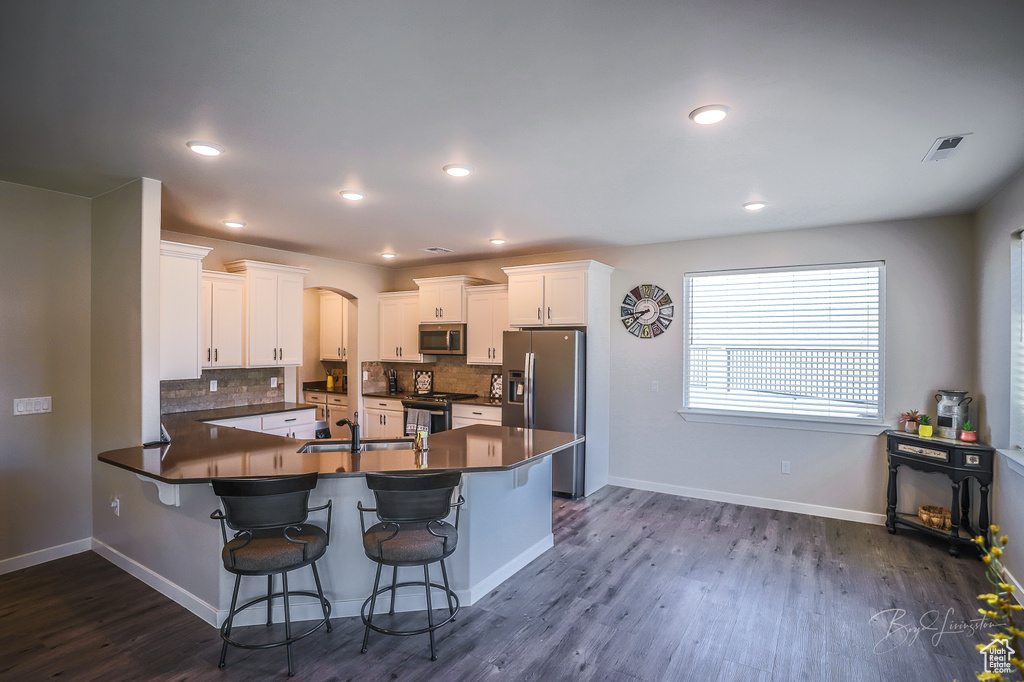 Kitchen with dark wood-type flooring, white cabinetry, appliances with stainless steel finishes, a kitchen breakfast bar, and kitchen peninsula