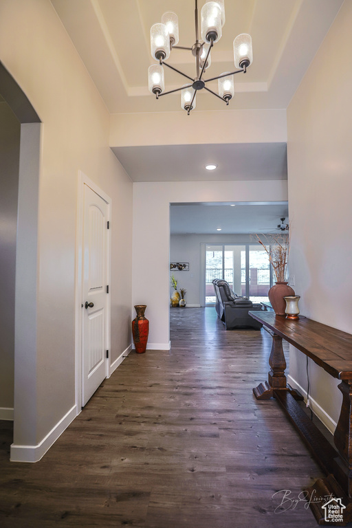 Hall with a raised ceiling, dark wood-type flooring, and a chandelier
