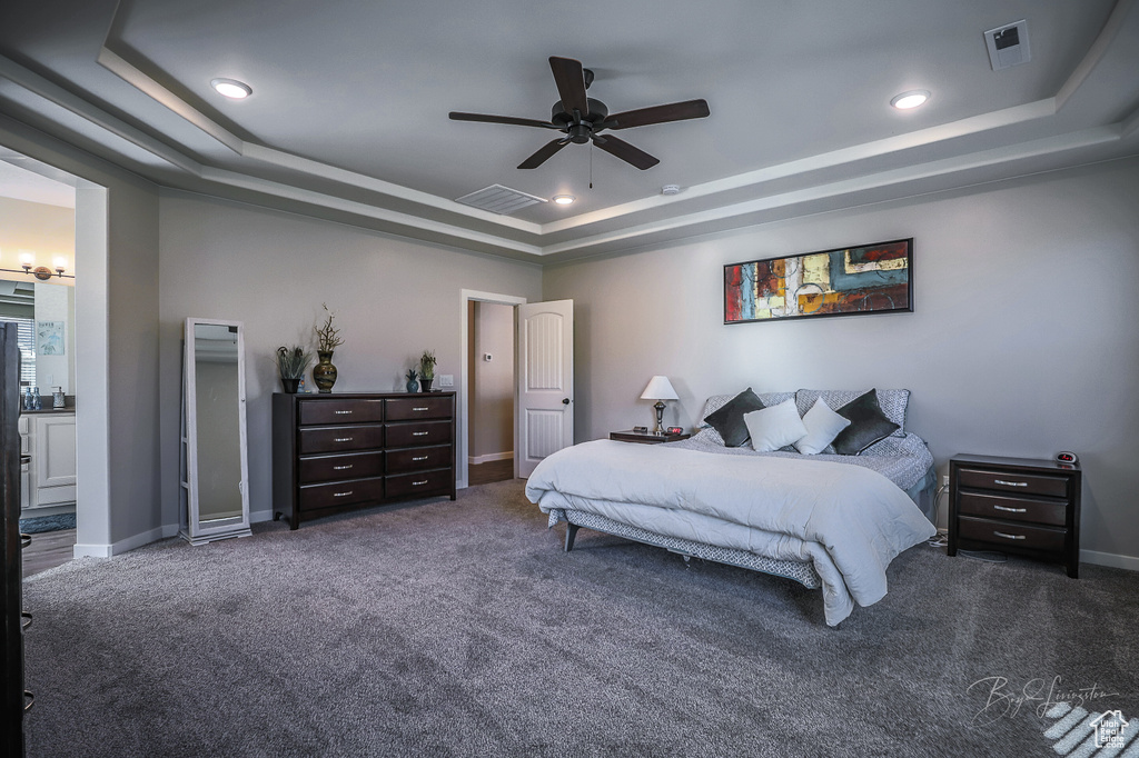 Carpeted bedroom featuring a raised ceiling, ceiling fan, and ensuite bathroom