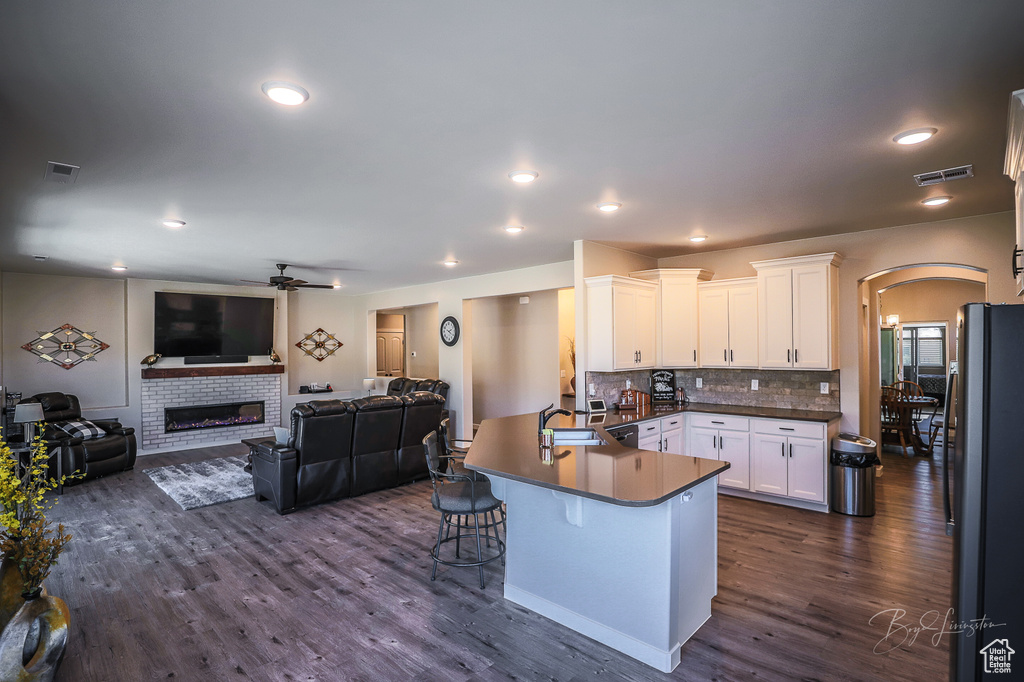 Kitchen with a breakfast bar, black refrigerator, dark hardwood / wood-style floors, white cabinetry, and kitchen peninsula