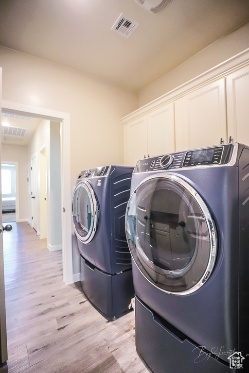 Clothes washing area with light hardwood / wood-style floors, cabinets, and washing machine and clothes dryer