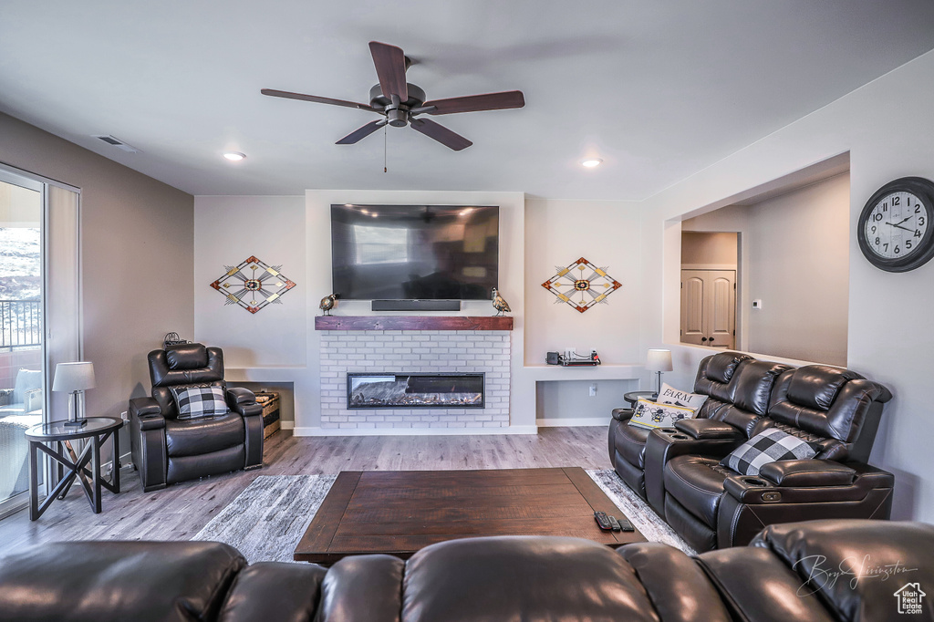 Living room with a fireplace, light hardwood / wood-style flooring, and ceiling fan