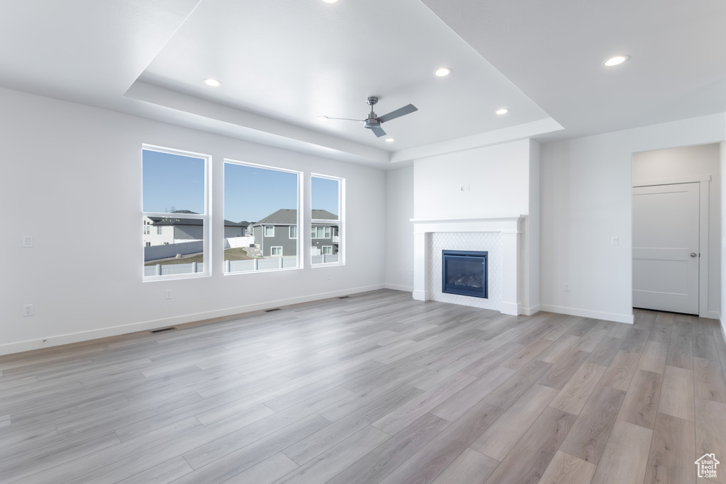 Unfurnished living room with a tiled fireplace, a tray ceiling, light hardwood / wood-style floors, and ceiling fan