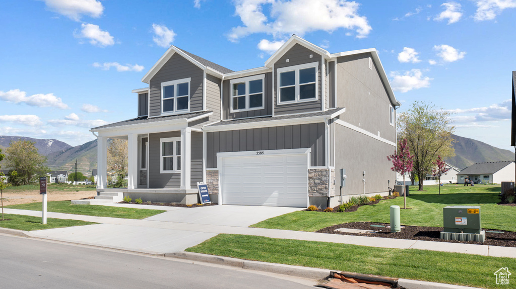 View of front of home with a mountain view, an attached garage, concrete driveway, a front lawn, and stone siding