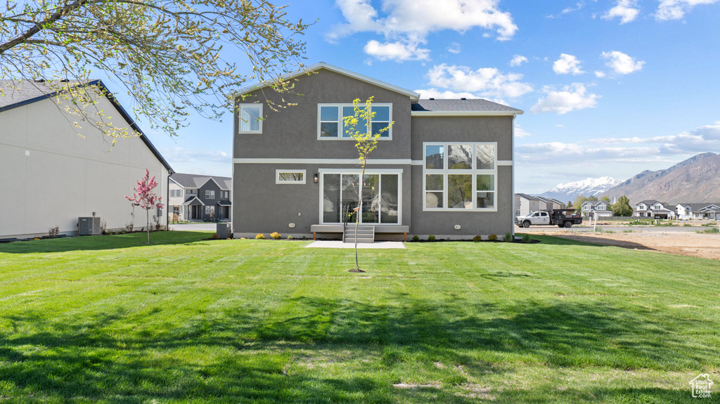 Rear view of house with a lawn, a mountain view, stucco siding, and central air condition unit