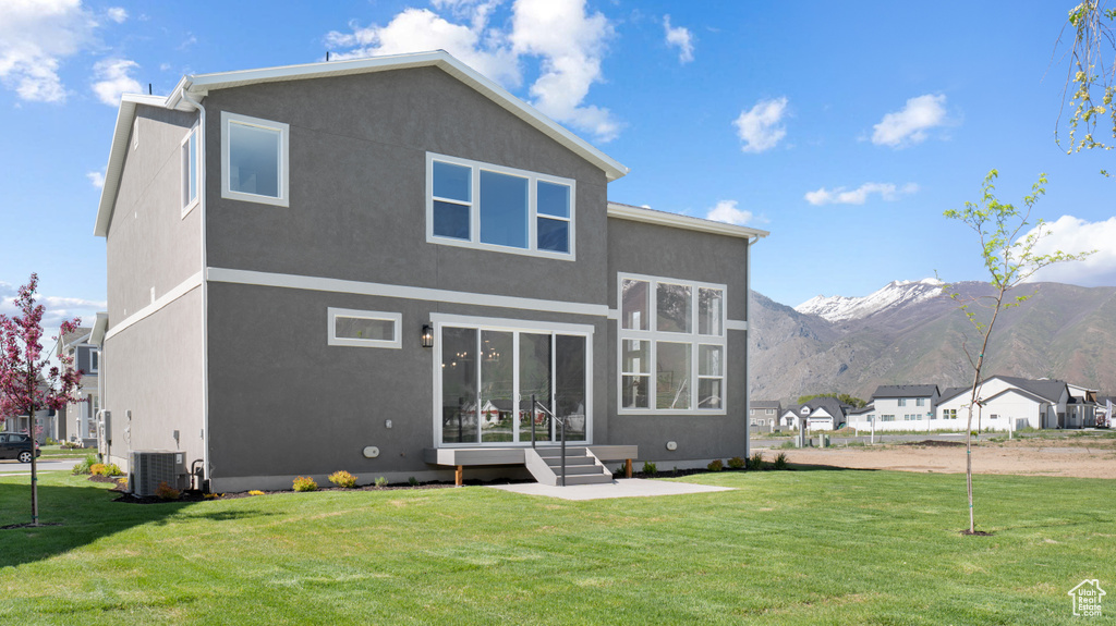 Rear view of house featuring central air condition unit, a lawn, stucco siding, and a mountain view