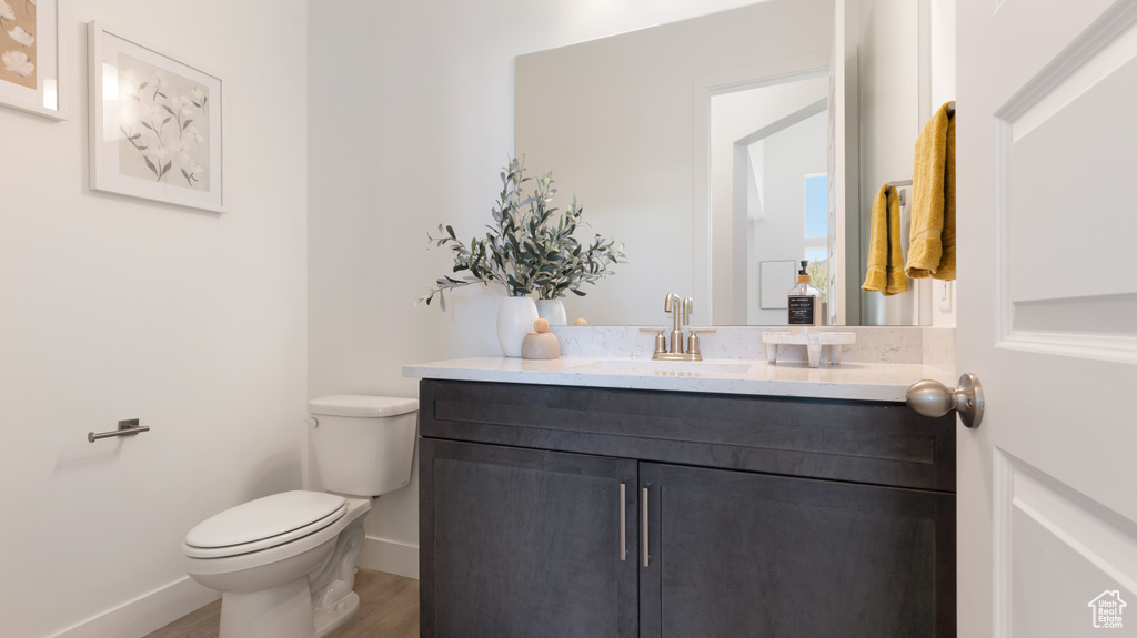 Bathroom with wood finished floors, toilet, vanity, and baseboards
