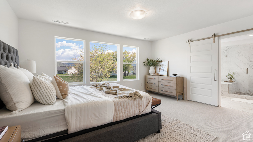Bedroom with a barn door, light colored carpet, and ensuite bathroom