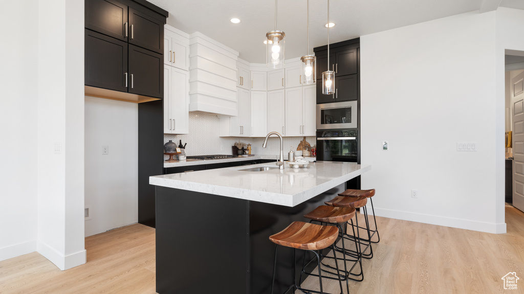 Kitchen with a sink, appliances with stainless steel finishes, light wood-type flooring, baseboards, and pendant lighting