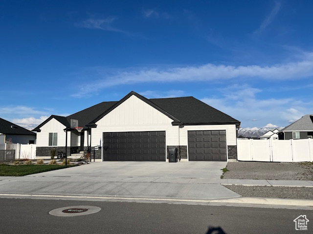 Modern farmhouse style home with an attached garage, stone siding, fence, a gate, and driveway
