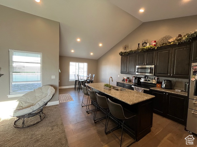 Kitchen with appliances with stainless steel finishes, wood finished floors, a sink, a center island with sink, and a breakfast bar area
