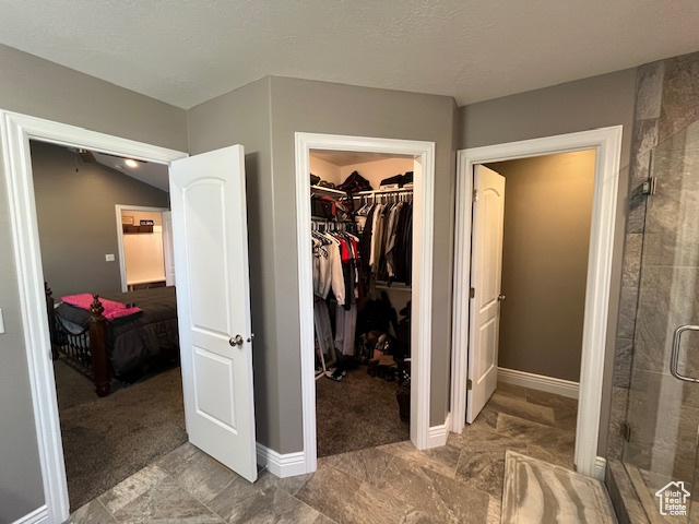 Interior space with a spacious closet, a stall shower, baseboards, and a textured ceiling