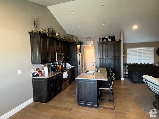 Kitchen featuring appliances with stainless steel finishes, lofted ceiling, sink, a kitchen bar, and a kitchen island with sink