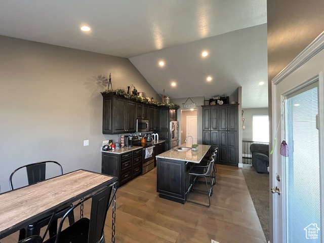 Kitchen featuring an island with sink, a kitchen bar, a sink, lofted ceiling, and stainless steel appliances