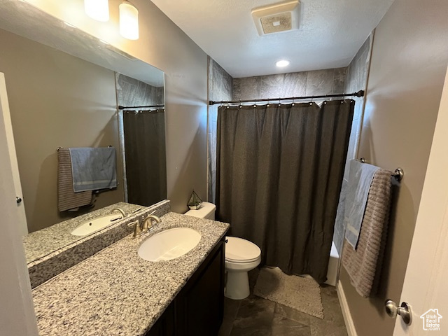 Full bath with a textured ceiling, vanity, visible vents, toilet, and shower / bath combo