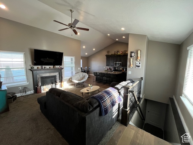 Living room with baseboards, a ceiling fan, a fireplace, wood finished floors, and vaulted ceiling