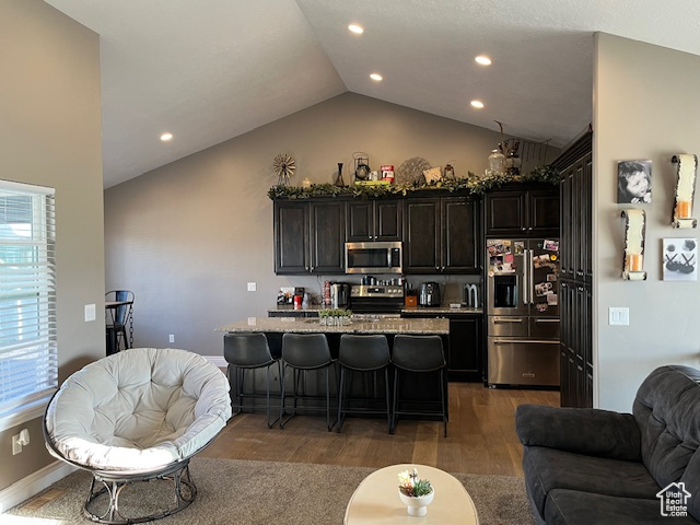 Kitchen featuring a breakfast bar, wood finished floors, lofted ceiling, stainless steel appliances, and open floor plan