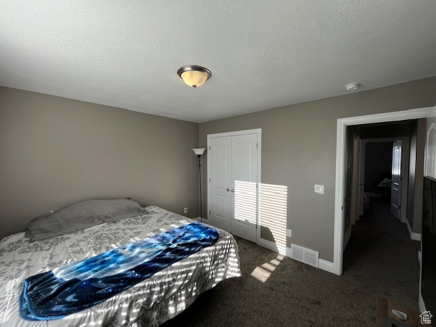 Bedroom with dark colored carpet, a closet, baseboards, a textured ceiling, and visible vents
