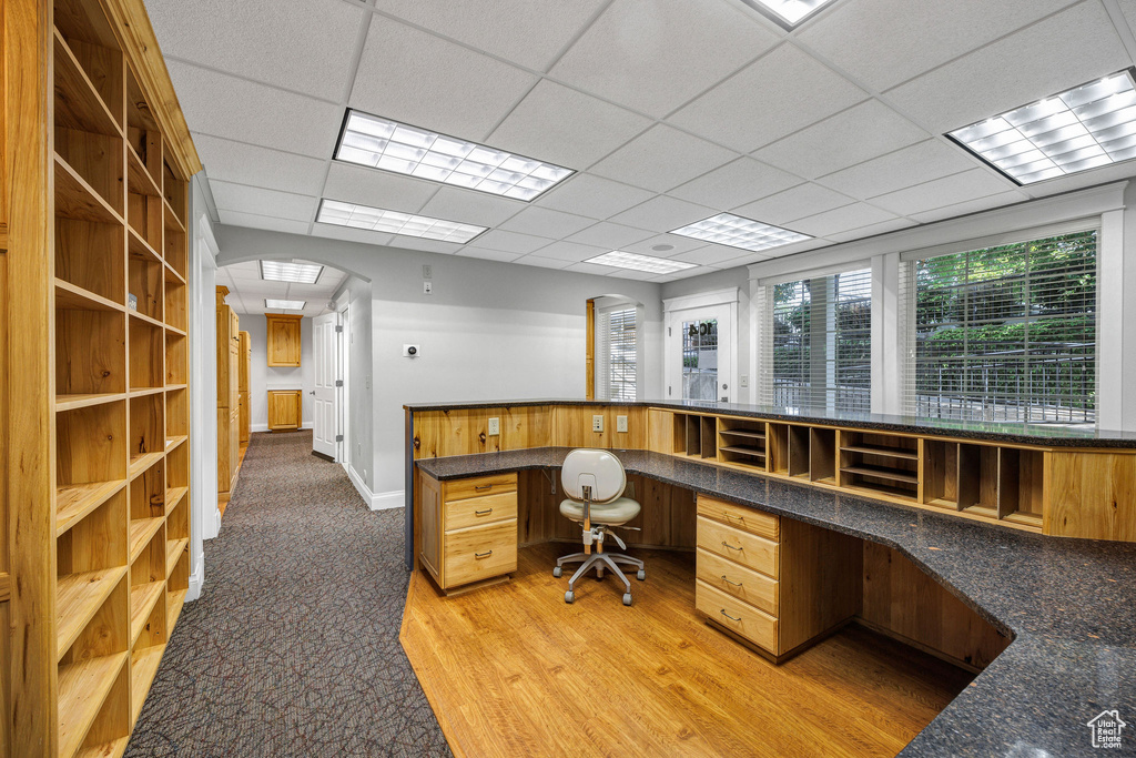 Office space featuring arched walkways, built in study area, a drop ceiling, light wood-type flooring, and light colored carpet