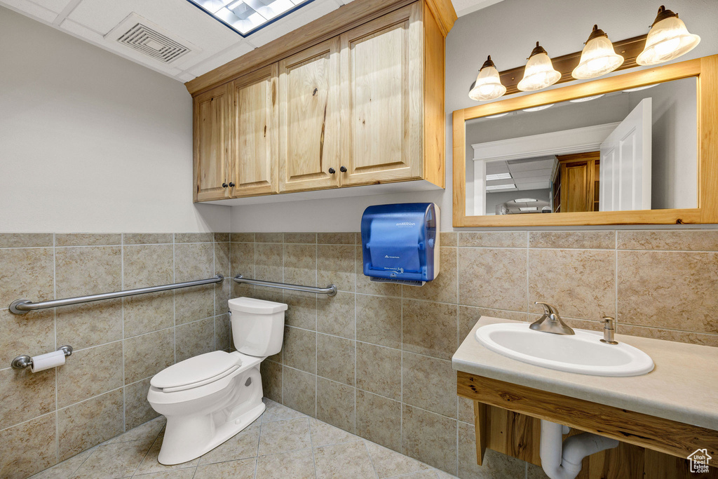 Half bathroom with tile walls, tile patterned floors, and wainscoting