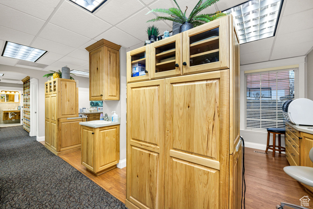 Kitchen with sink, ornate columns, light brown cabinets, light hardwood / wood-style floors, and a drop ceiling