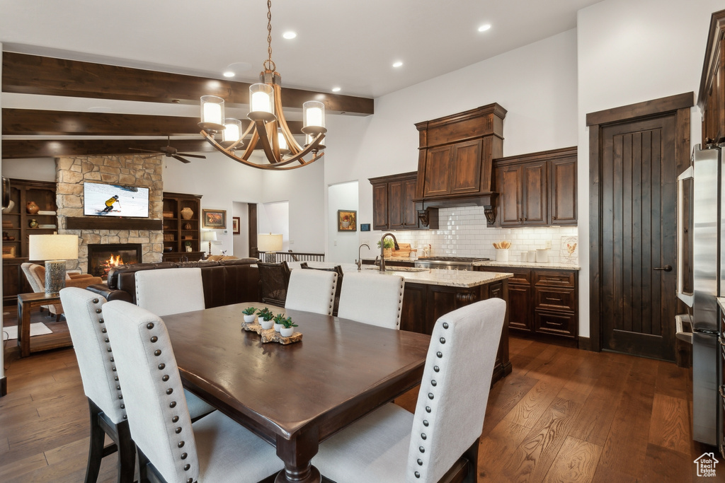 Dining space with a stone fireplace, sink, high vaulted ceiling, dark hardwood / wood-style floors, and beam ceiling