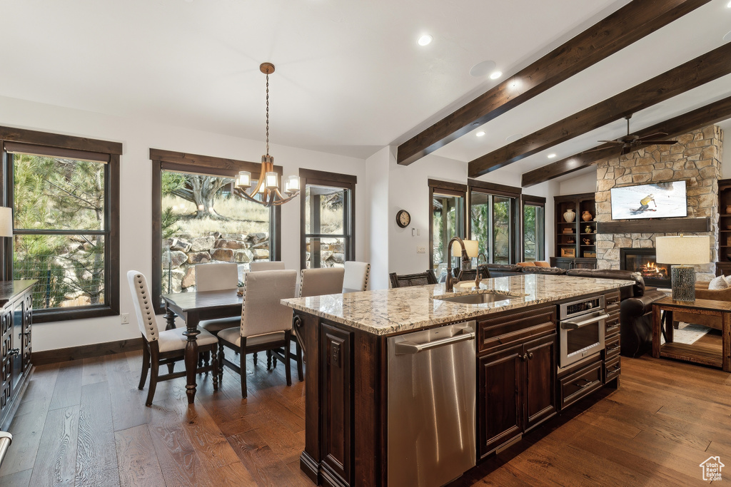 Kitchen featuring sink, appliances with stainless steel finishes, light stone countertops, an island with sink, and decorative light fixtures