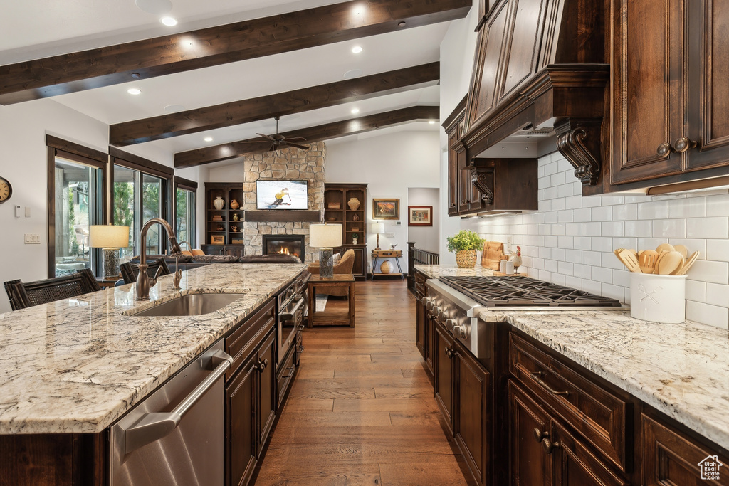 Kitchen with stainless steel appliances, sink, vaulted ceiling with beams, and light stone counters