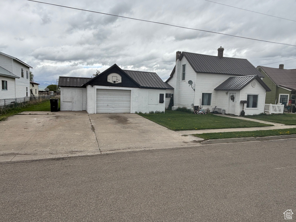 View of front of house featuring metal roof, concrete driveway, a chimney, and an outbuilding