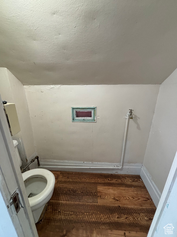 Bathroom with wood-type flooring, a textured ceiling, vaulted ceiling, and toilet