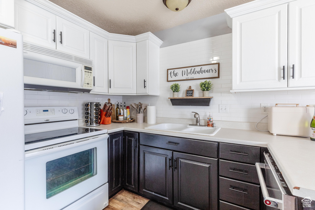 Kitchen featuring tasteful backsplash, sink, white cabinets, white appliances, and a textured ceiling