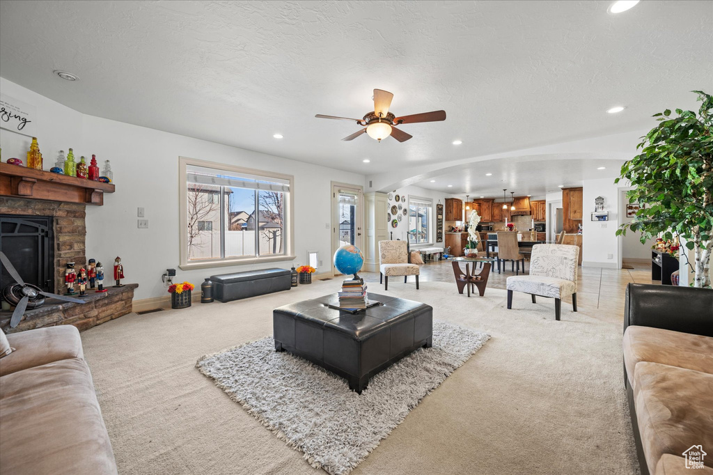 Carpeted living room featuring ceiling fan, a textured ceiling, a fireplace, and a healthy amount of sunlight