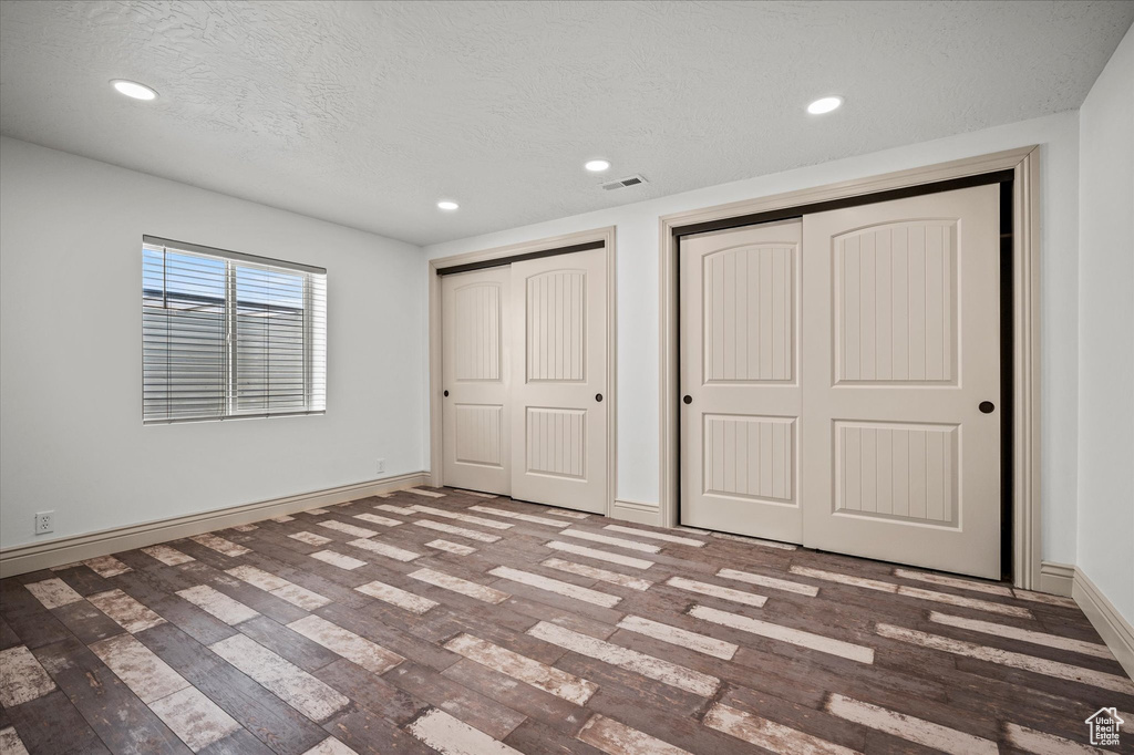 Unfurnished bedroom with multiple closets, a textured ceiling, and hardwood / wood-style flooring