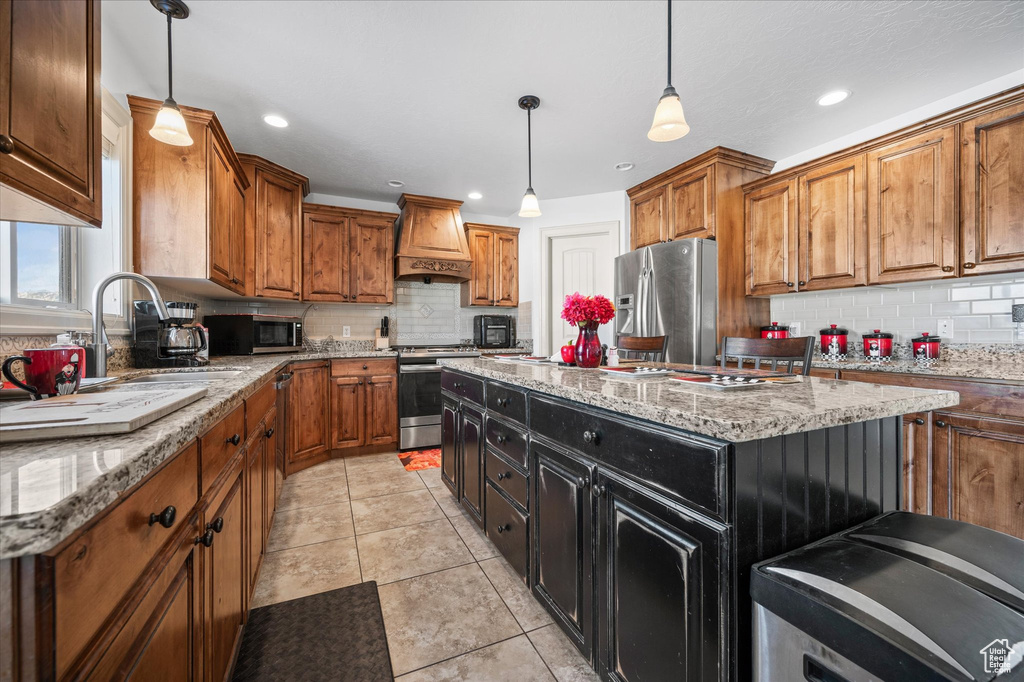 Kitchen featuring premium range hood, light stone counters, a kitchen island, pendant lighting, and stainless steel appliances