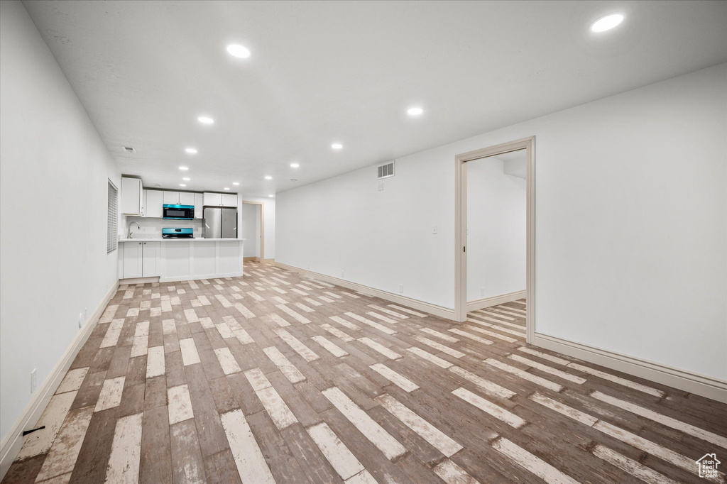 Basement with stainless steel refrigerator and light wood-type flooring