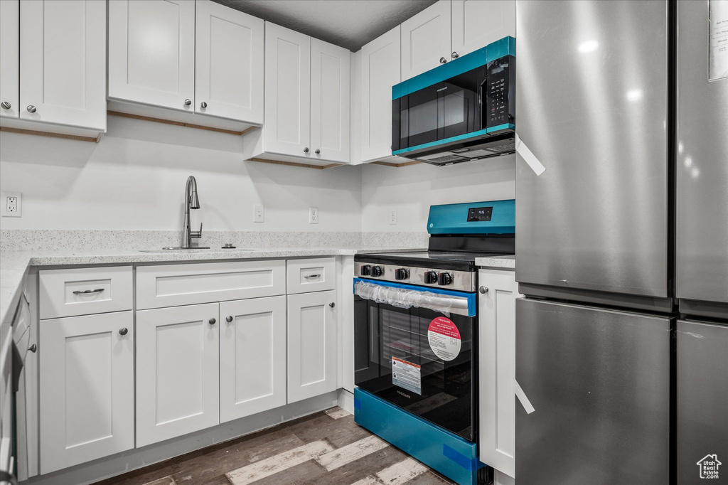 Kitchen with sink, stainless steel appliances, white cabinets, and light stone countertops