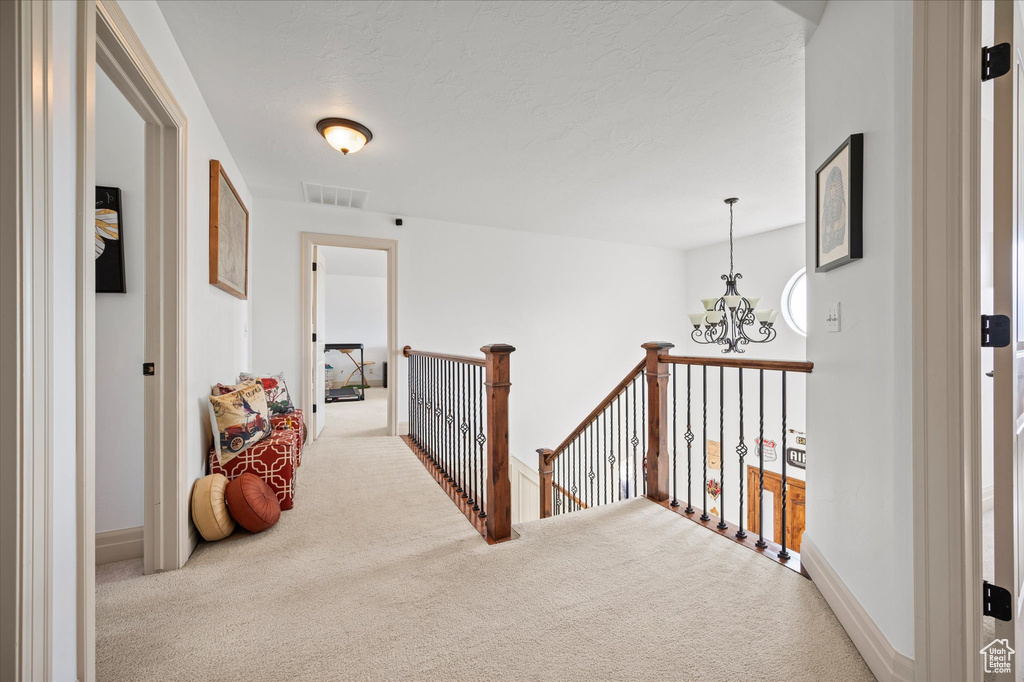 Hall with light carpet, a notable chandelier, and a textured ceiling