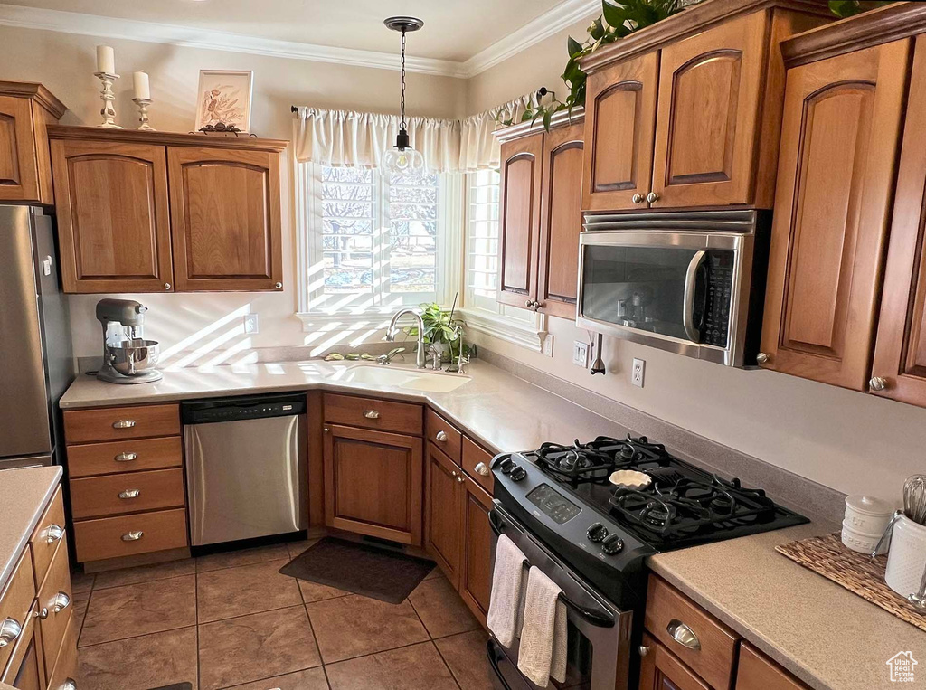 Kitchen with decorative light fixtures, sink, ornamental molding, stainless steel appliances, and tile patterned floors