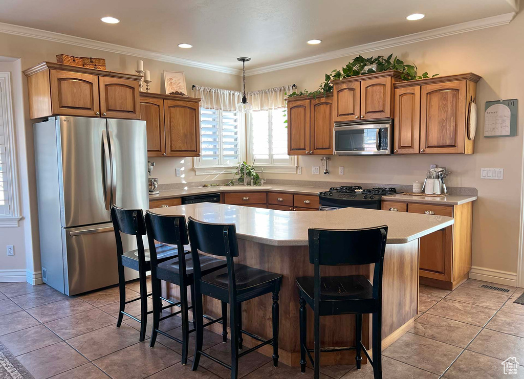 Kitchen with crown molding, a breakfast bar, hanging light fixtures, a center island, and black appliances