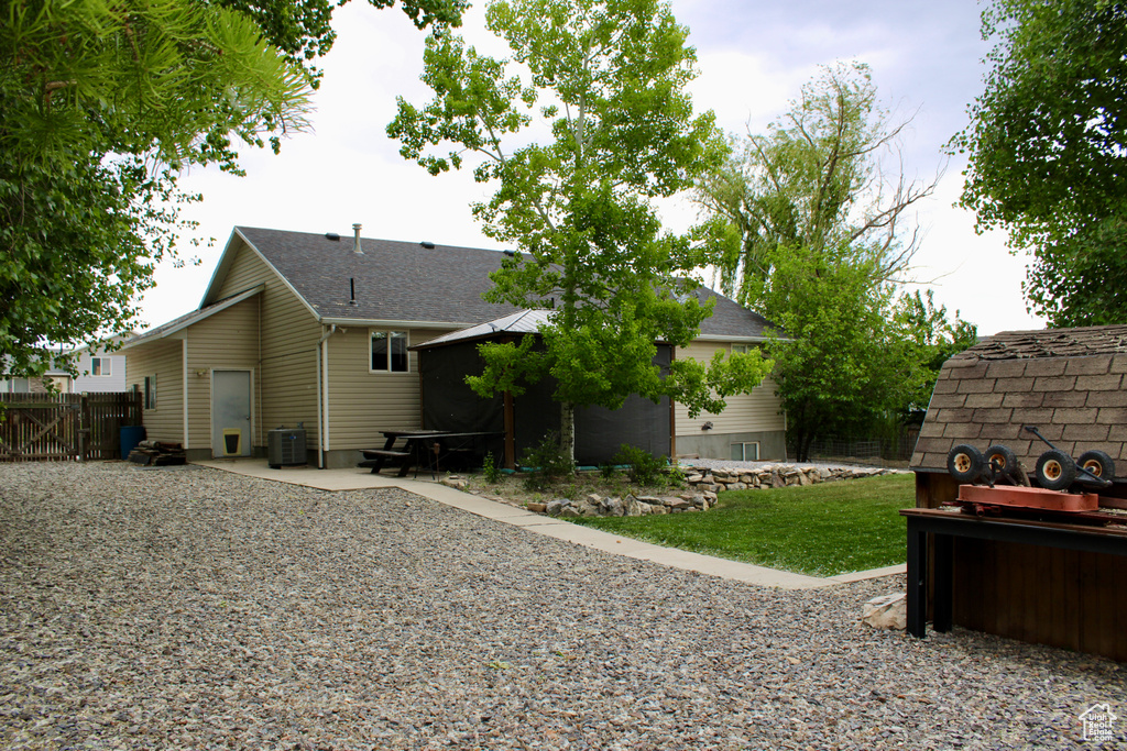 Back of property with central air condition unit, a patio area, and roof with shingles