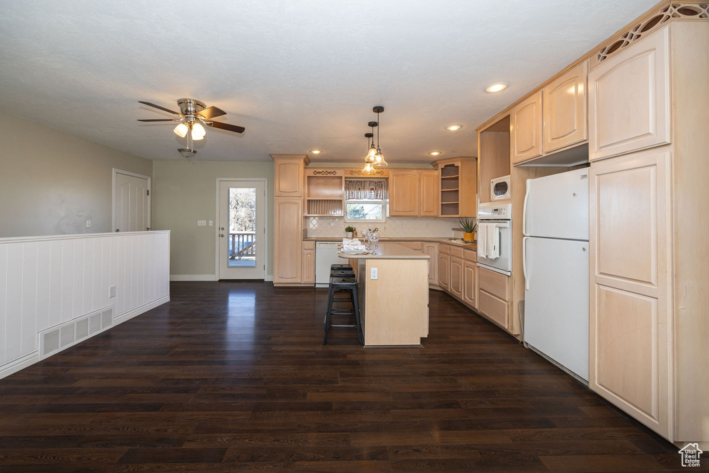 Kitchen featuring a kitchen island, dark hardwood / wood-style floors, a kitchen breakfast bar, hanging light fixtures, and white appliances