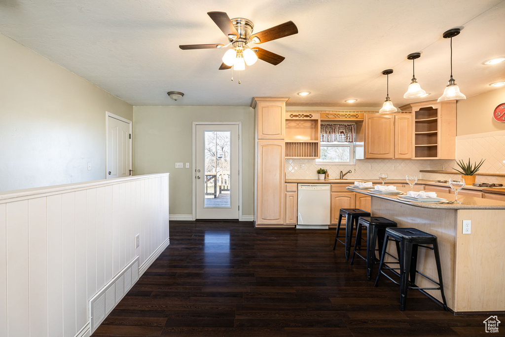 Kitchen featuring dark wood-type flooring, a kitchen breakfast bar, white dishwasher, decorative light fixtures, and light brown cabinets