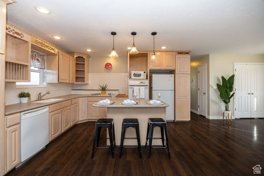 Kitchen with a breakfast bar, sink, a center island, dark wood-type flooring, and white appliances