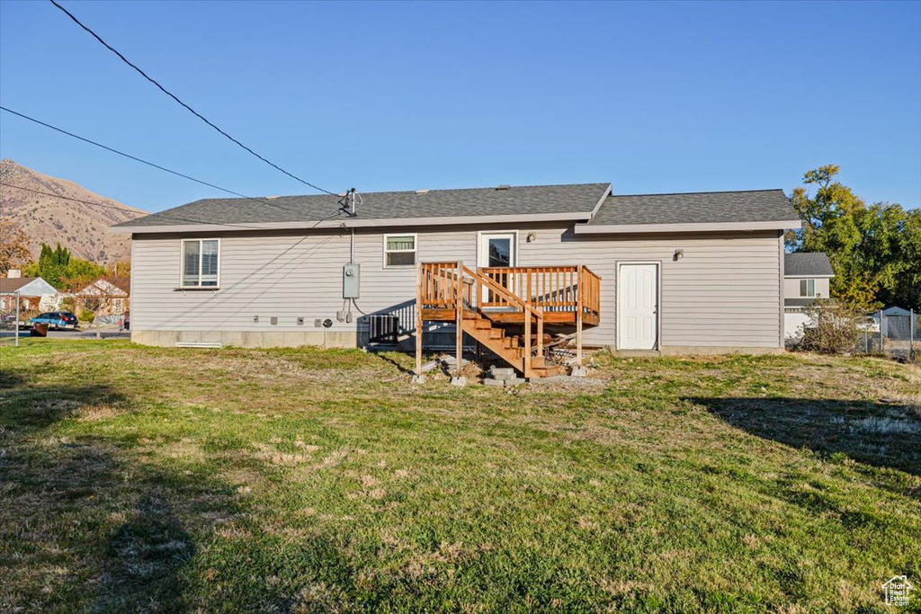 Rear view of property featuring cooling unit, a deck with mountain view, and a lawn